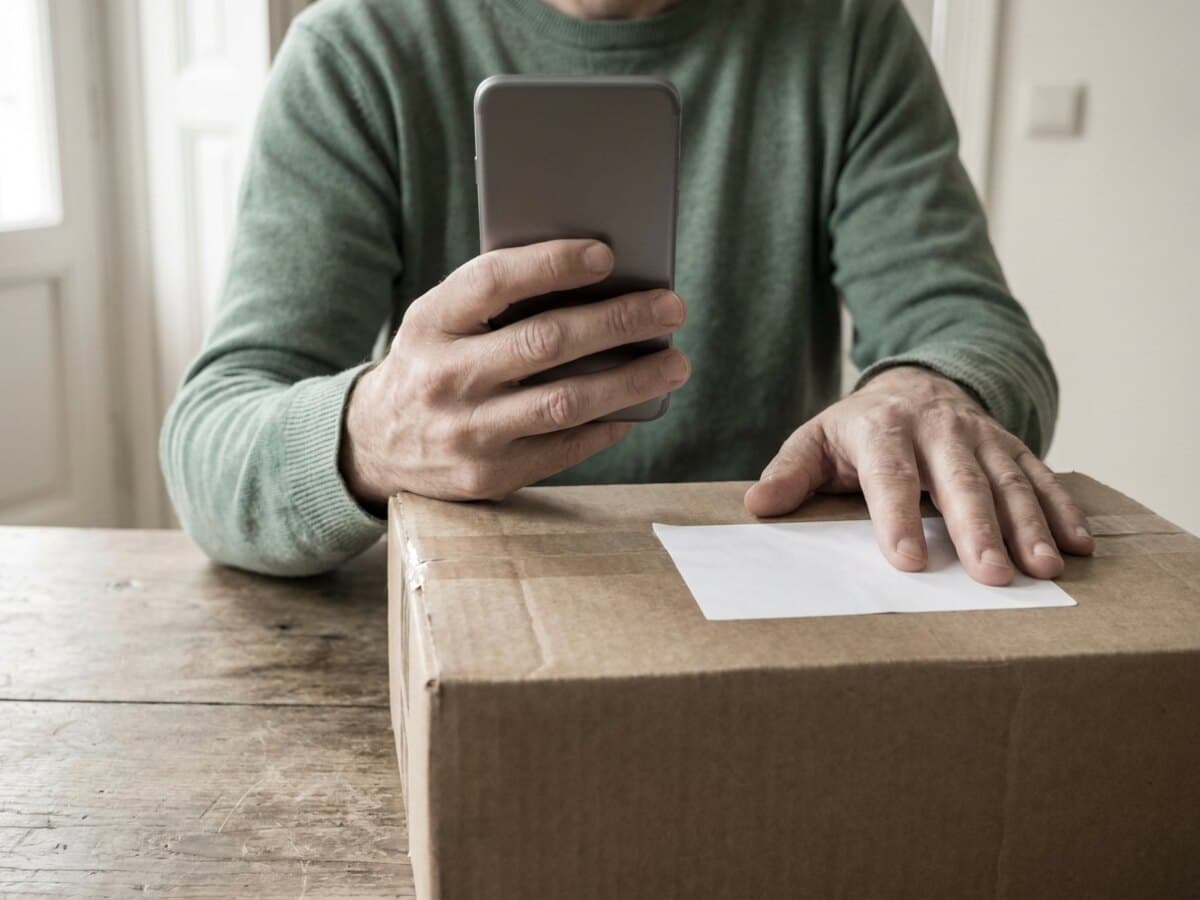 A customer at home with the sealed parcel on the table, reading something on their phone.