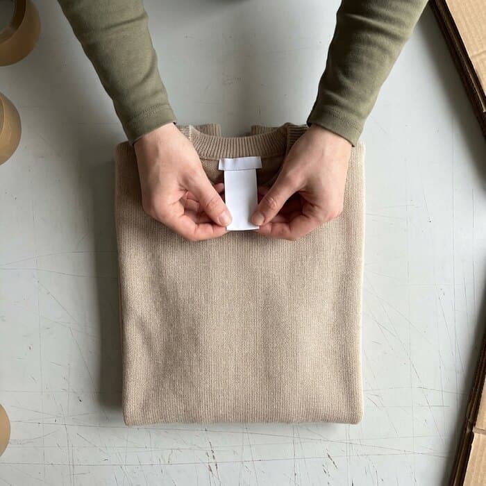 A folded knitted sweater with its care tags shown to the camera on the packing bench